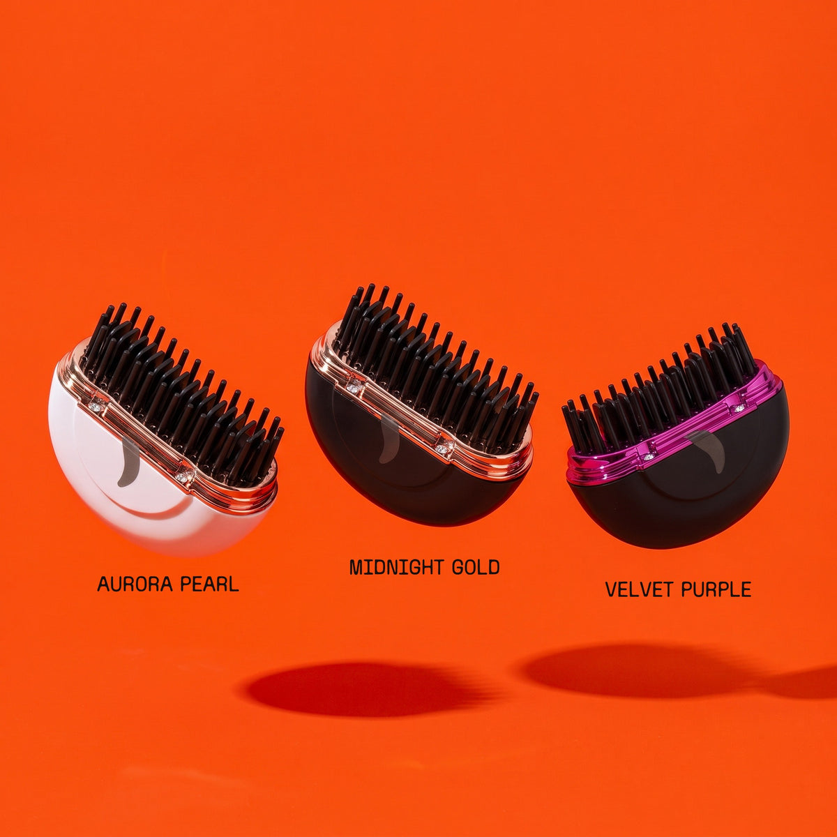 Le tre finiture della HairSnapper Brush sospese su fondo arancio: Aurora Pearl, Midnight Gold e Velvet Purple