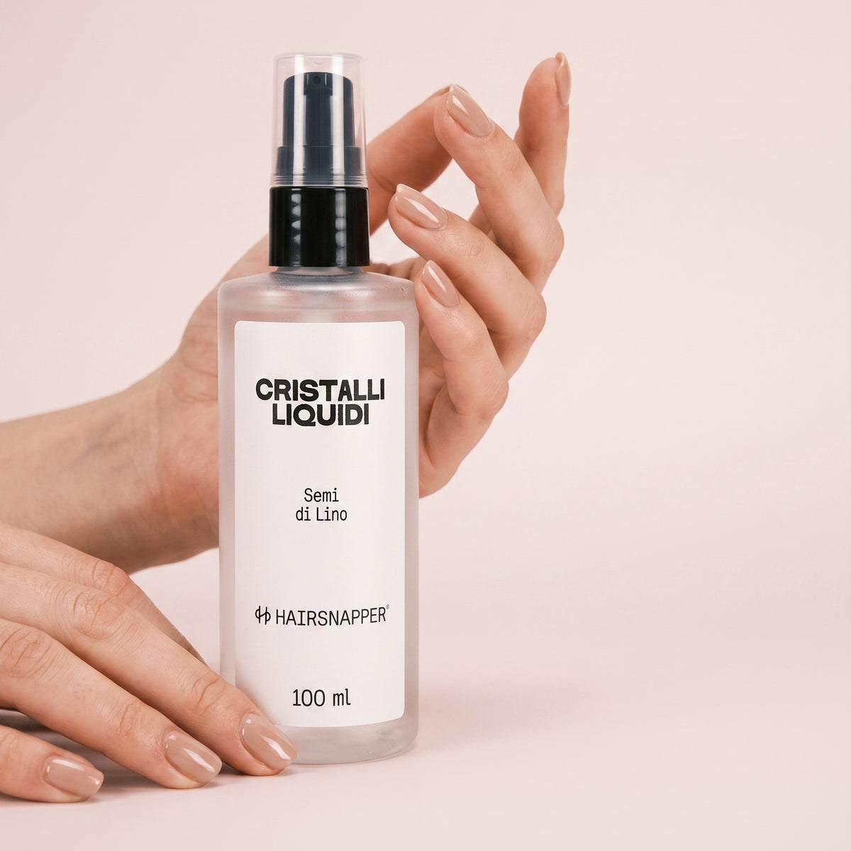 HairSnapper Cristalli Liquidi 100 ml tenuti fra due mani su fondo cipria