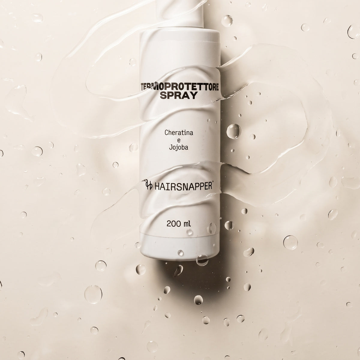 HairSnapper Termoprotettore Spray 200 ml visto dall'alto fra gocce d'acqua su fondo avorio