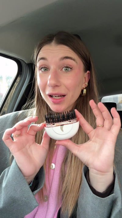Una ragazza in auto tiene la HairSnapper Brush aperta in mano e si sistema i capelli lunghi.